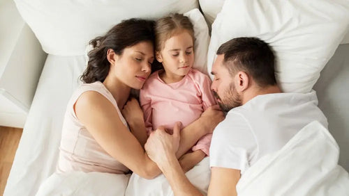 Family co-sleeping in white bedding — parenting tips and family sleep guides from OZI Sleep