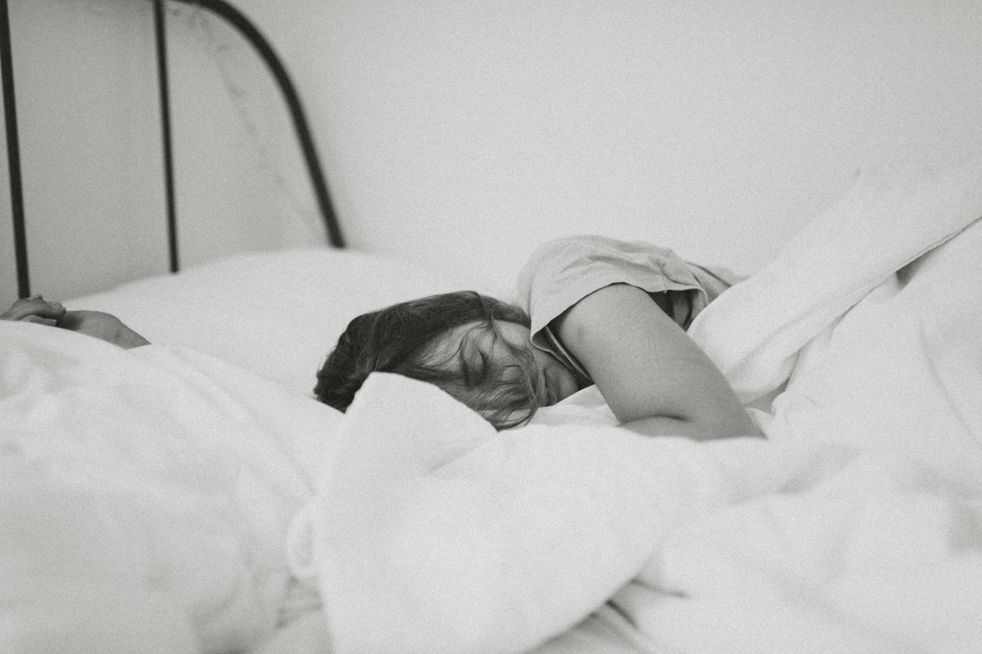 Adult sleeping deeply in white bedding (black-and-white) — the restful nights OZI Sleep helps families achieve