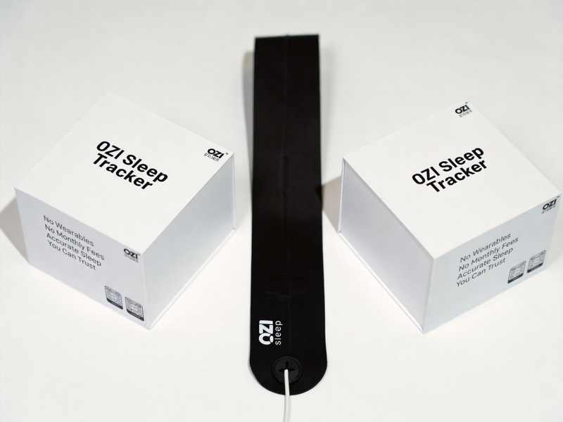 Two OZI Sleep Tracker boxes flanking the under-sheet sensor strip — product packaging shot