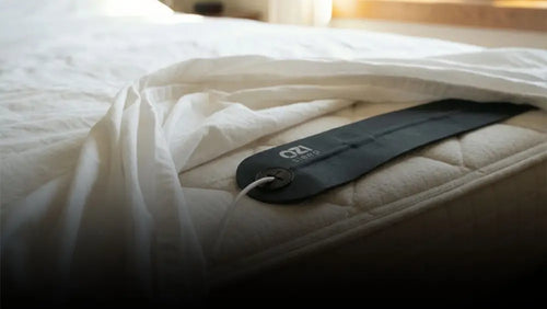 OZI Sleep Tracker sensor strip placed under the sheet on a mattress — non-wearable sleep technology in action